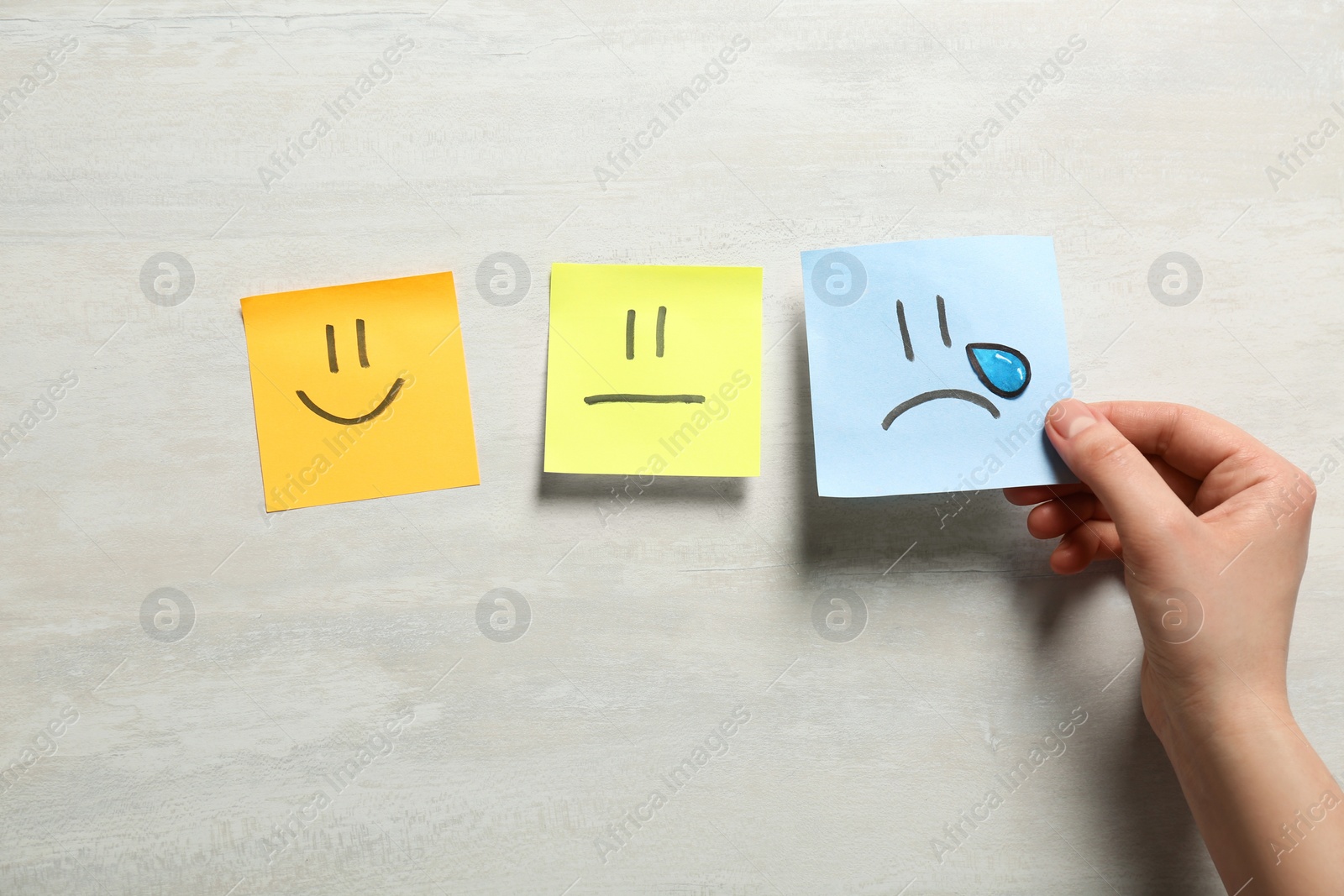 Photo of Woman holding sticker with sad face on light background, closeup