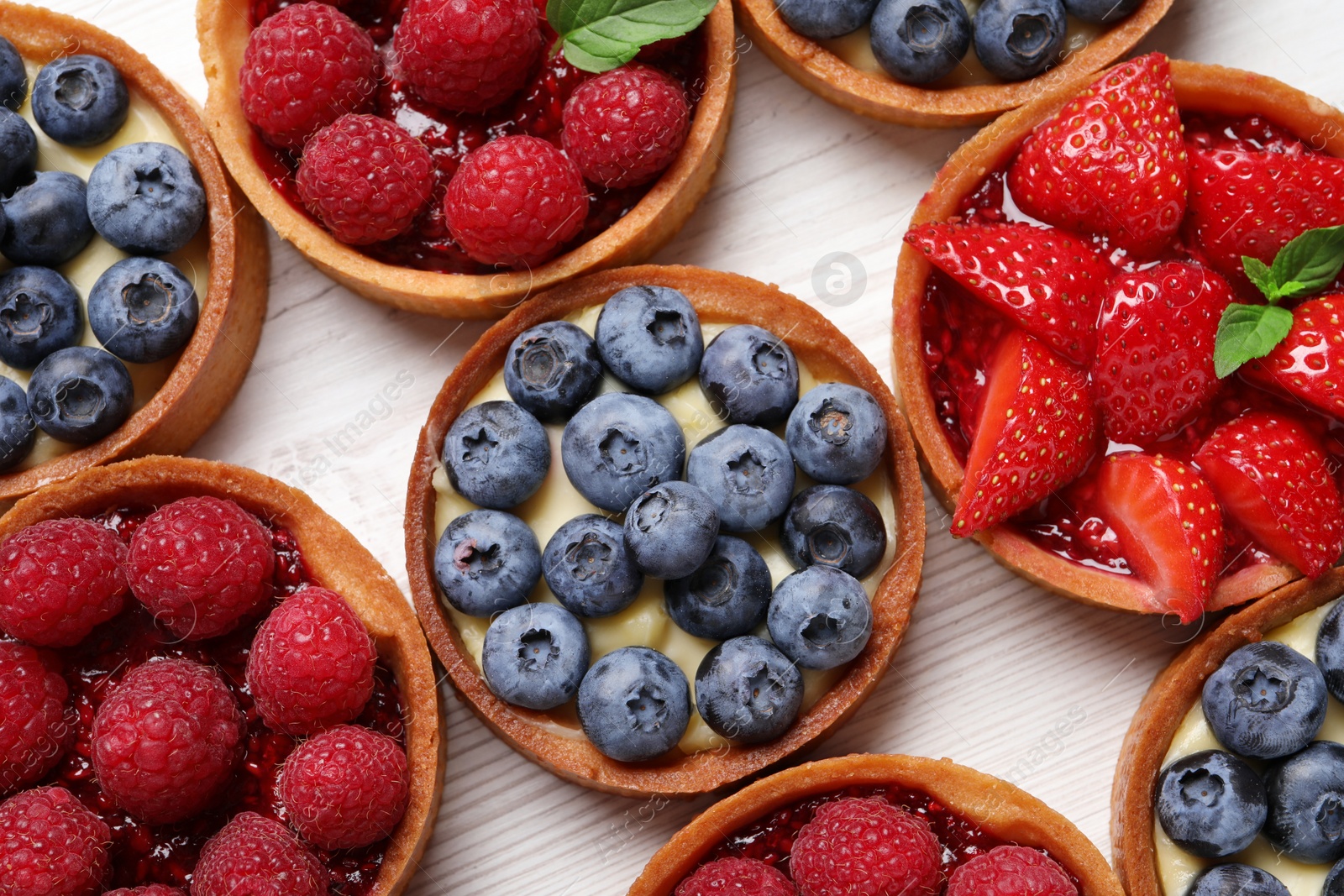 Photo of Tartlets with different fresh berries on white wooden table, flat lay. Delicious dessert