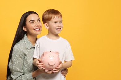 Photo of Mother and her son with ceramic piggy bank on orange background, space for text