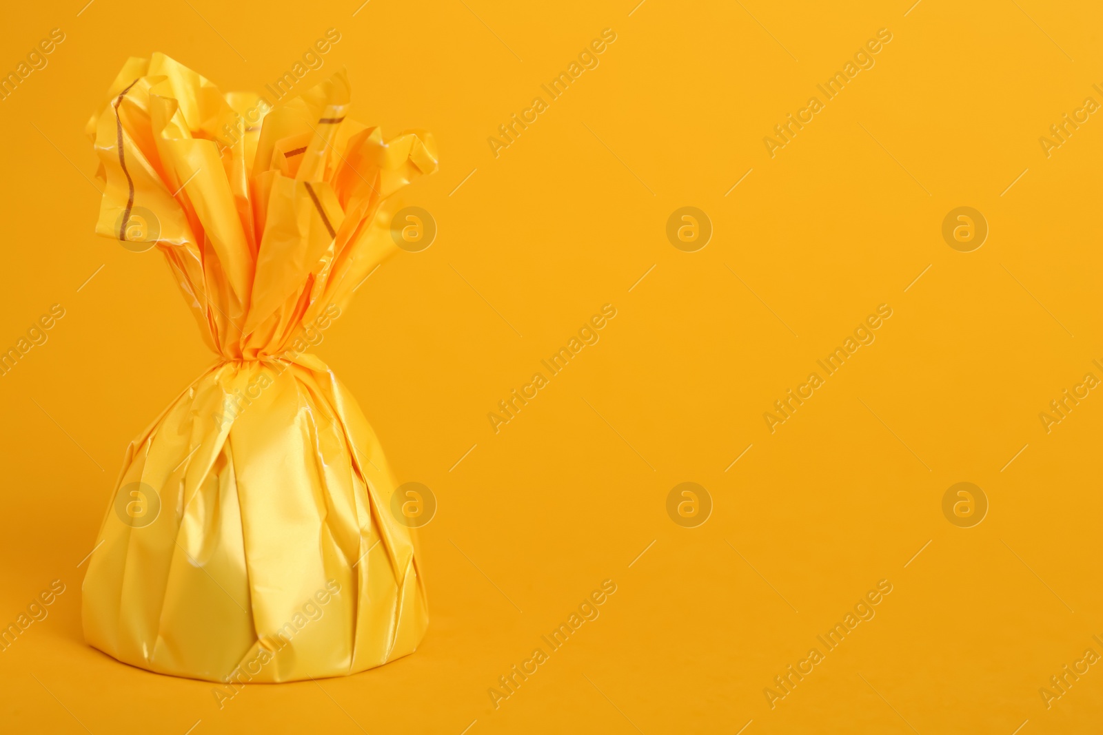 Photo of Candy in bright wrapper on yellow background. Space for text