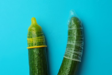 Photo of Cucumbers with condoms on light blue background, flat lay. Safe sex concept