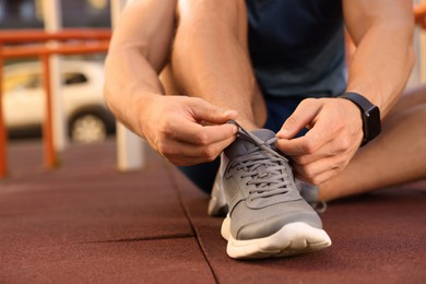 Photo of Man tying shoelaces before training at outdoor gym, closeup