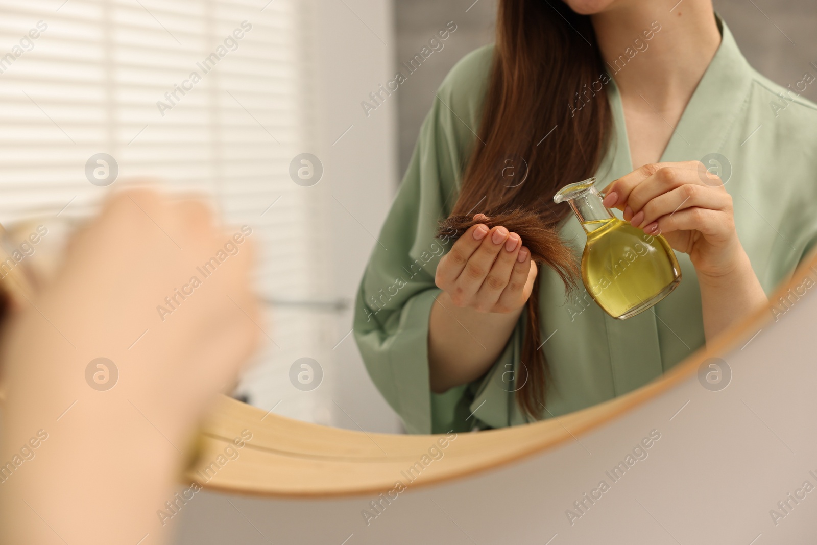 Photo of Woman applying oil hair mask near mirror at home, closeup