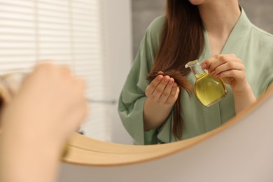 Photo of Woman applying oil hair mask near mirror at home, closeup
