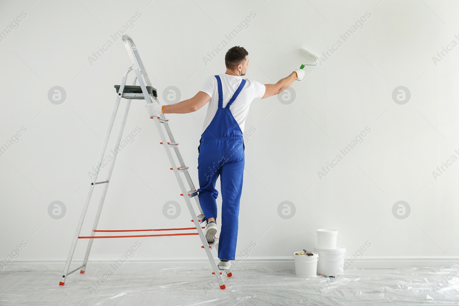 Photo of Man painting wall with white dye indoors, back view