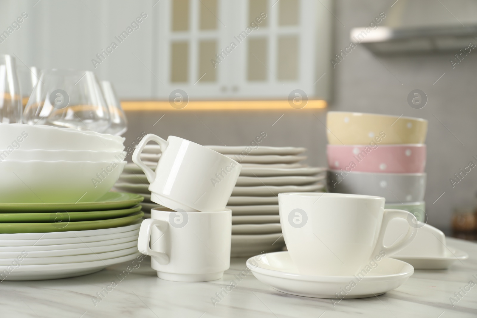 Photo of Clean plates, bowls, cups and glasses on white marble table in kitchen