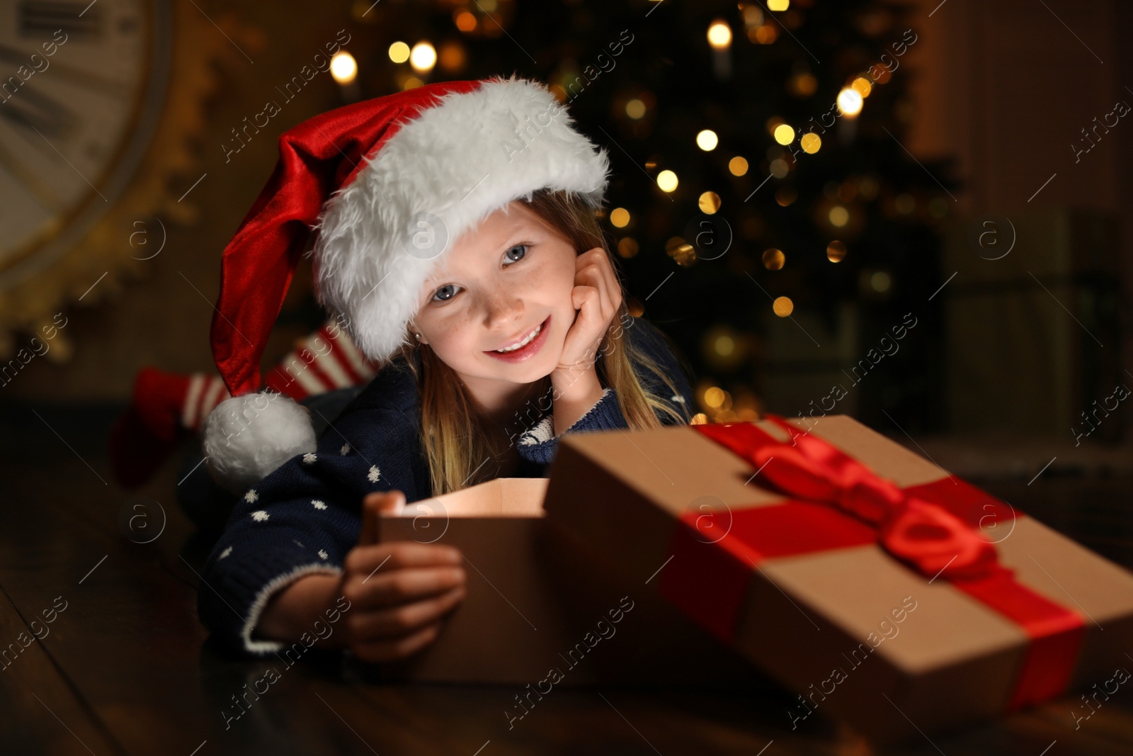 Photo of Cute child opening magic gift box near Christmas tree at night