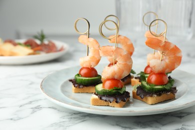 Photo of Tasty canapes with shrimps, cucumber, greens and tomatoes on white marble table, closeup