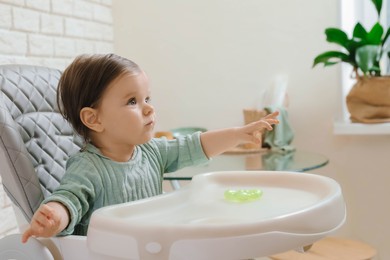 Cute little baby sitting in high chair indoors