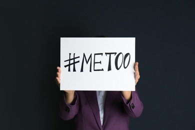 Photo of Woman holding paper with text "#METOO" on dark background. Problem of sexual harassment at work