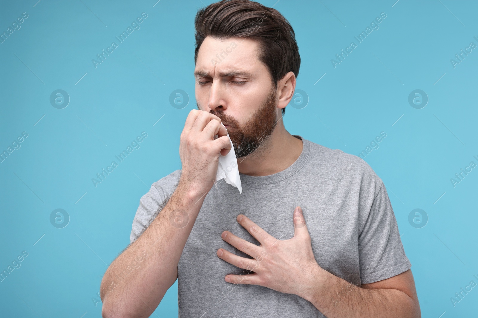 Photo of Sick man with tissue coughing on light blue background