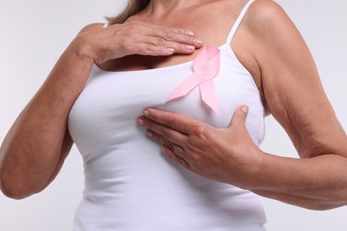 Photo of Woman with pink ribbon on white background, closeup. Breast cancer awareness