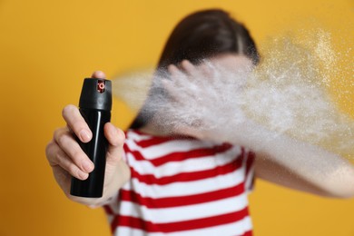 Young woman covering eyes with hand and using pepper spray on yellow background