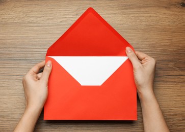 Photo of Woman opening red letter at wooden table, top view