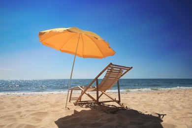 Photo of Orange beach umbrella and deck chair on sandy seashore
