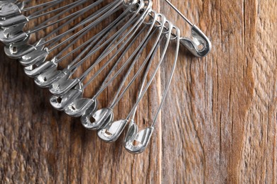 Many safety pins on wooden table, flat lay. Space for text