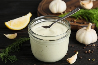 Photo of Composition with jar of garlic sauce on wooden table