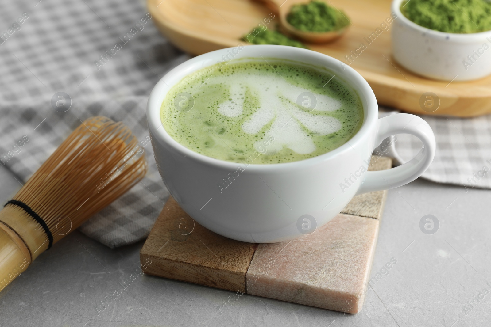 Photo of Cup of fresh matcha latte and bamboo whisk on light grey table, closeup