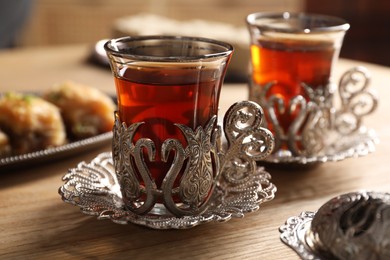 Photo of Glasses of traditional Turkish tea in vintage holders on wooden table, closeup