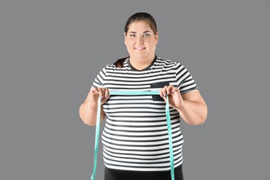 Overweight woman with measuring tape on gray background