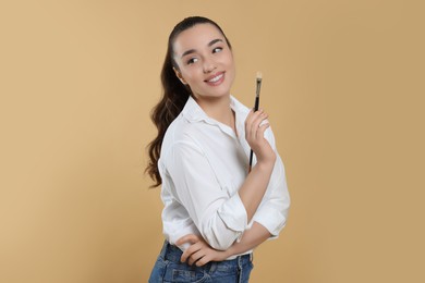 Photo of Woman with paintbrush on beige background. Young artist