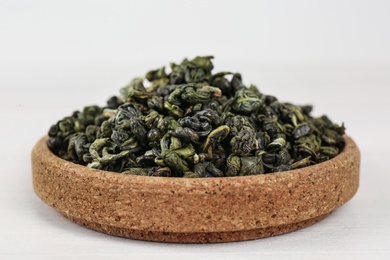 Photo of Dried green tea leaves in cork bowl on white table, closeup
