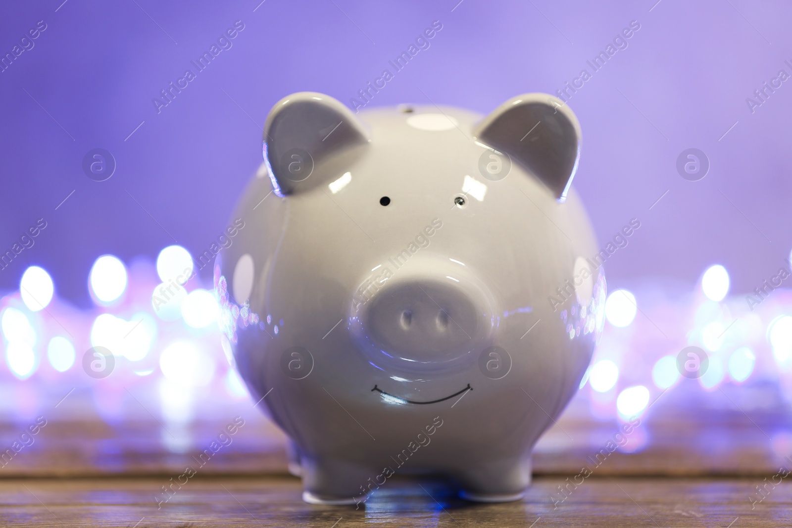 Photo of Cute piggy bank on table against blurred Christmas lights