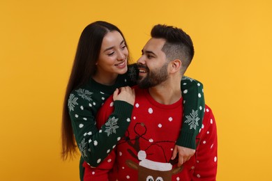 Photo of Happy young couple in Christmas sweaters on orange background