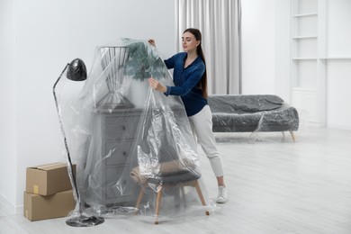 Photo of Young woman putting plastic film away from furniture at home