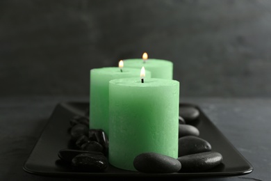 Dark plate with three burning candles and rocks on table