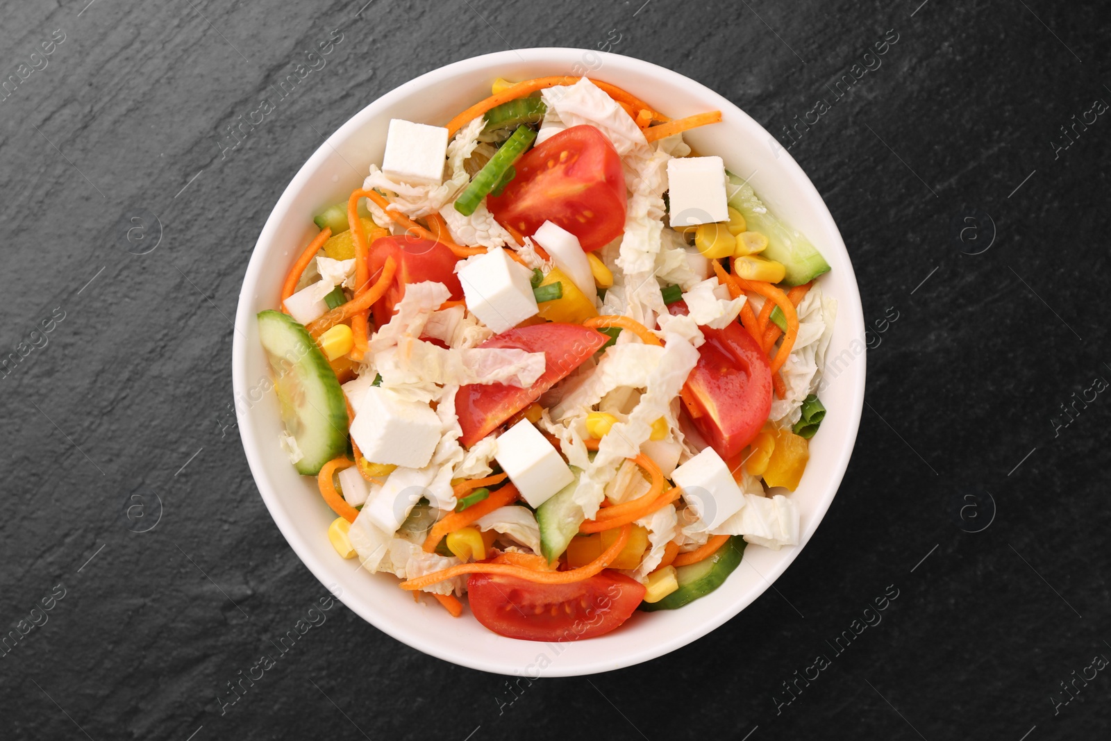 Photo of Tasty salad with Chinese cabbage, carrot, cheese, cucumber, corn and tomato on black table, top view