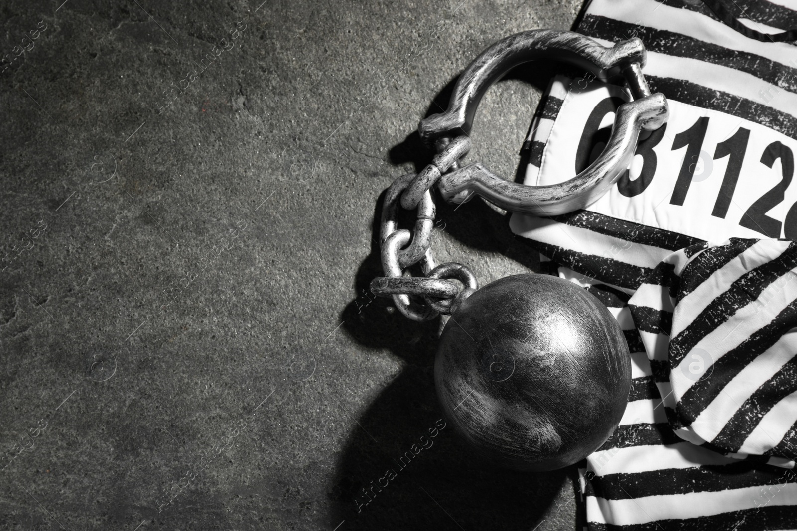 Photo of Prisoner ball with chain and jail clothes on grey table, flat lay. Space for text