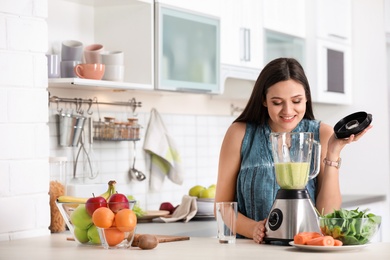 Photo of Young woman preparing tasty healthy smoothie at table in kitchen