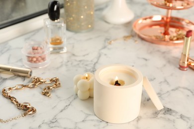 Burning soy candles, cosmetics and stylish accessories on white window sill indoors