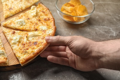 Photo of Man taking slice of delicious cheese pizza at table