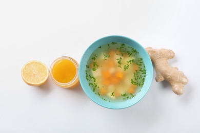 Photo of Bowl of fresh homemade soup to cure flu, lemon, ginger and honey on white background, top view