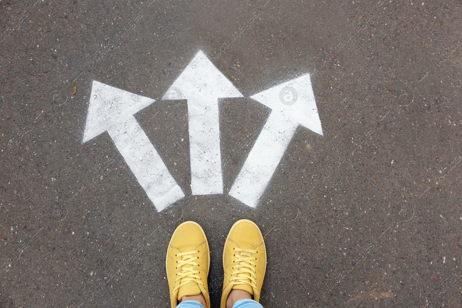 Photo of Woman standing near arrows on asphalt, top view. Choice concept