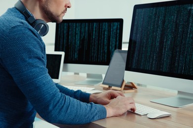 Photo of Programmer with headphones working at desk in office, closeup