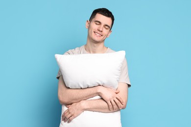 Photo of Happy man in pyjama holding pillow on light blue background