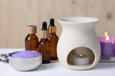 Photo of Different aromatherapy products and burning candles on white wooden table, closeup
