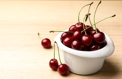 Photo of White bowl of delicious cherries on wooden table, space for text