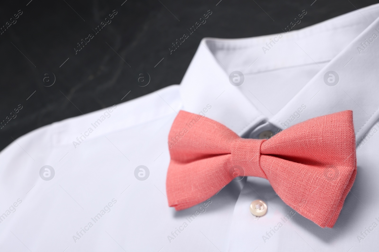 Photo of White shirt with stylish coral bow tie on grey background, closeup