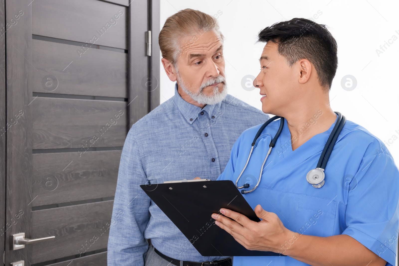 Photo of Doctor with clipboard consulting senior patient in clinic