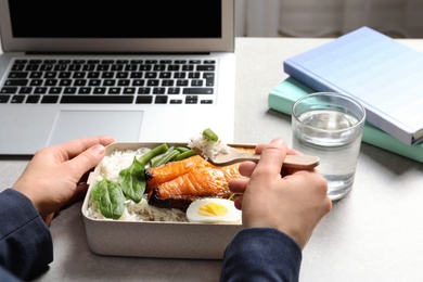 Woman eating natural protein food from container at office table