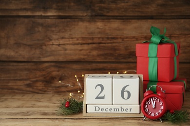 Photo of Block calendar with Boxing Day date, alarm clock and gifts on wooden background, space for text