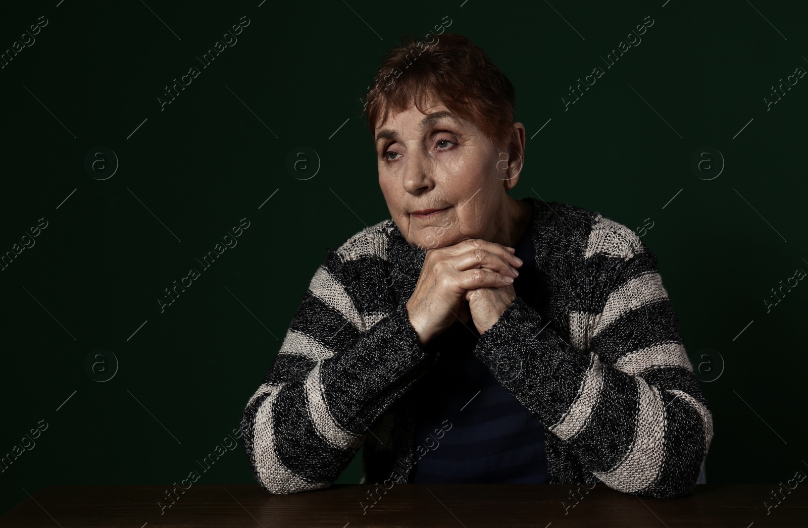 Photo of Poor senior woman sitting at table against color background. Space for text