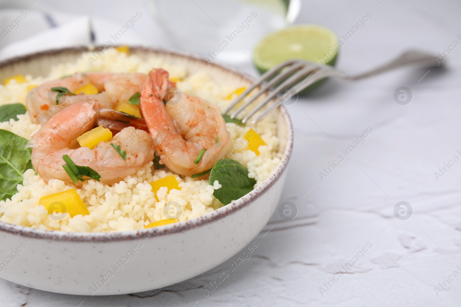 Photo of Tasty couscous with shrimps, bell pepper and basil on white textured table, closeup. Space for text