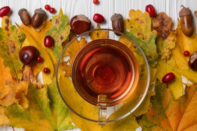 Different autumn leaves, acorns, chestnuts, red berries and cup of tasty tea on table, flat lay
