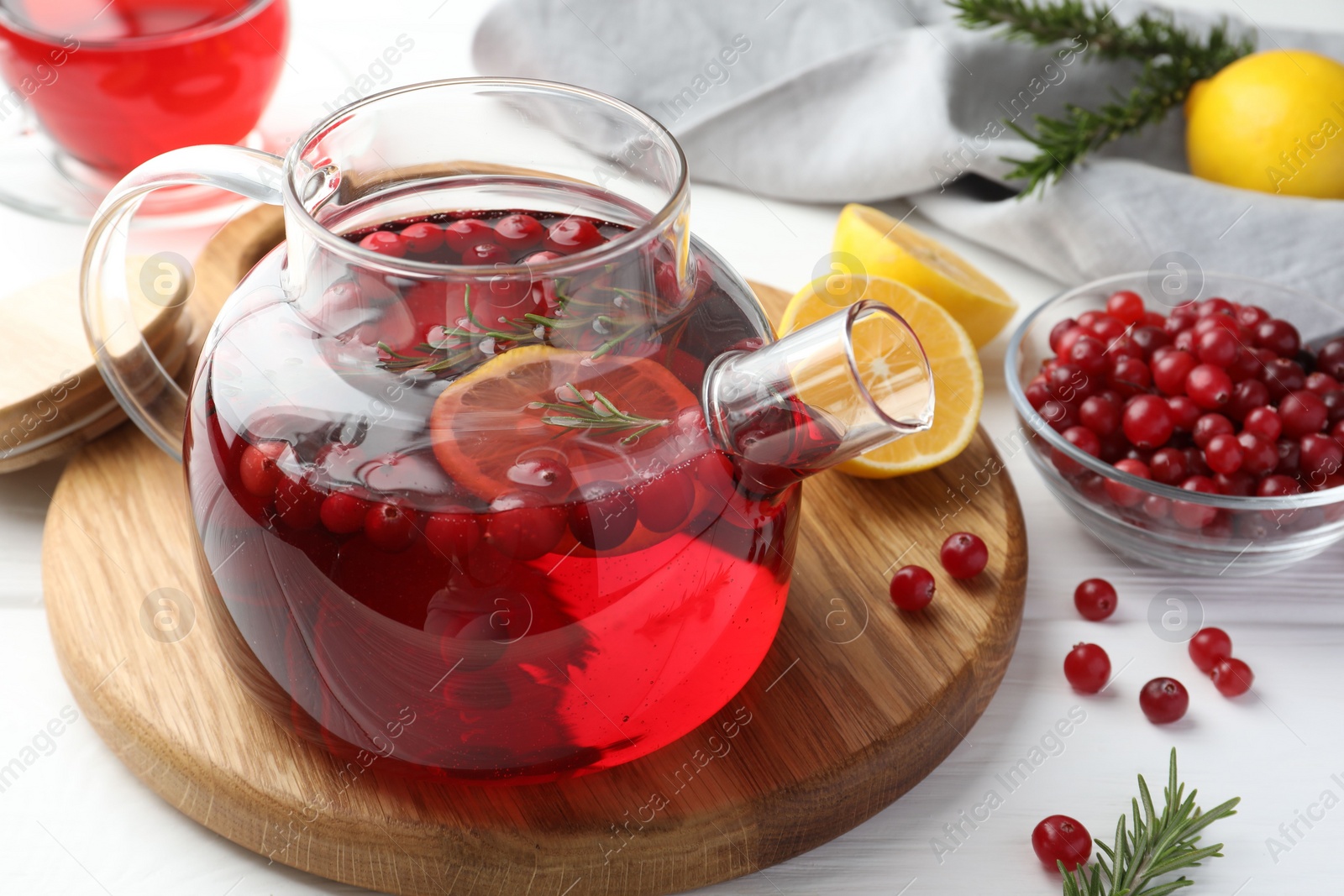 Photo of Tasty hot cranberry tea with lemon, rosemary and fresh berries in teapot on white wooden table