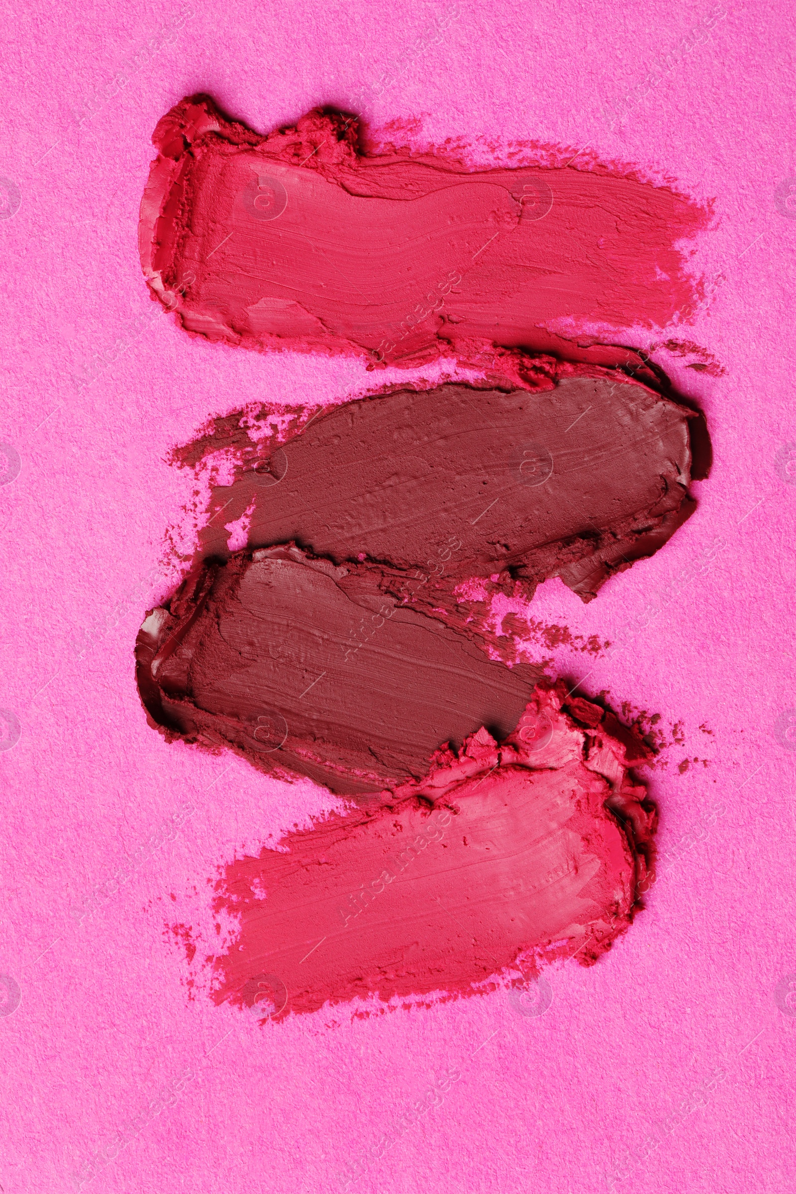 Photo of Smears of bright lipsticks on pink background, top view